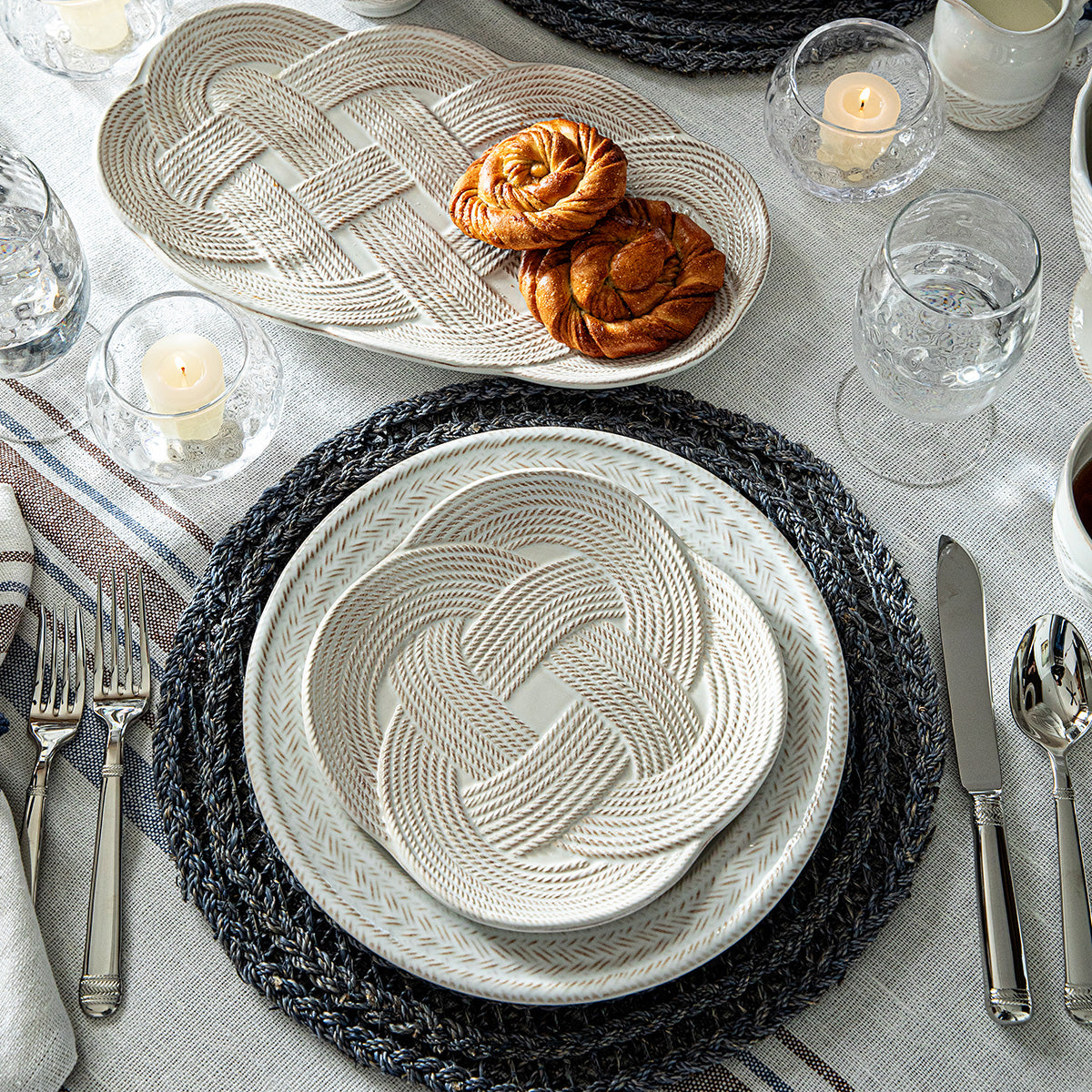 Navy Le Panier placemat under layered plates on a table set with pastries, candles, and glassware