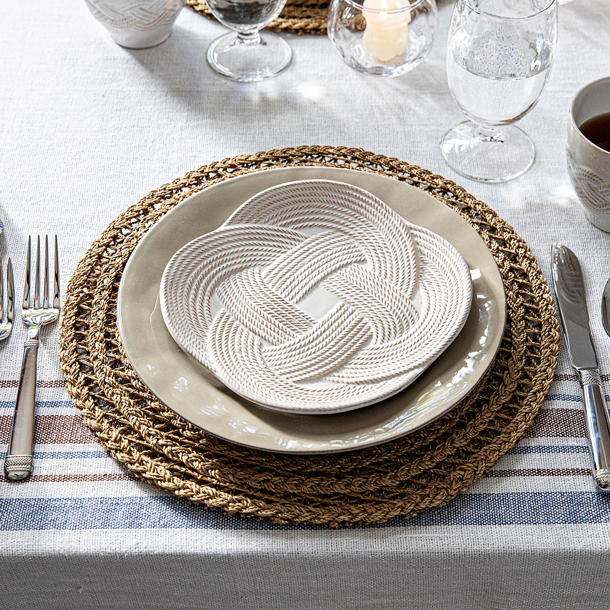 Overhead view of Le Panier Placemat in Taupe showcasing handwoven abaca texture with layered plates and glassware on a table