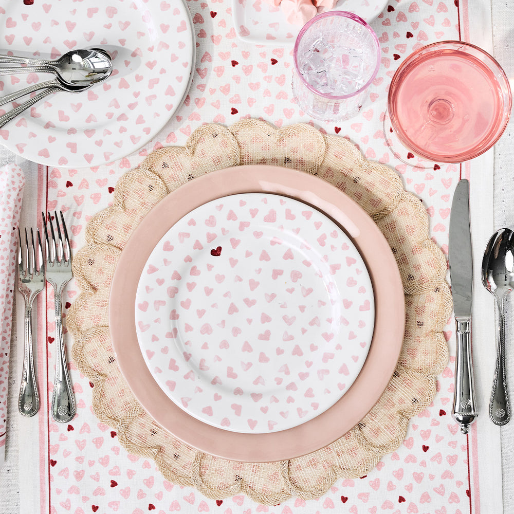 Top-down view of Heart Placemat in Natural showcasing scalloped woven abaca texture and embroidered heart detail on a heart-patterned table setting