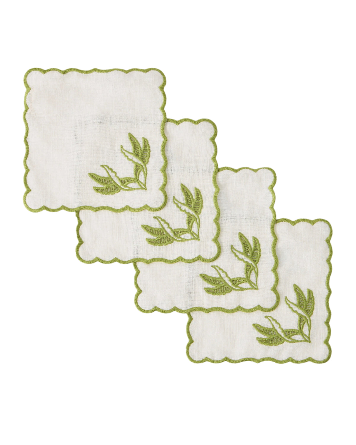 Overhead view of four DESTREE x Cabana cocktail napkins with scalloped edges and green floral embroidery on white
