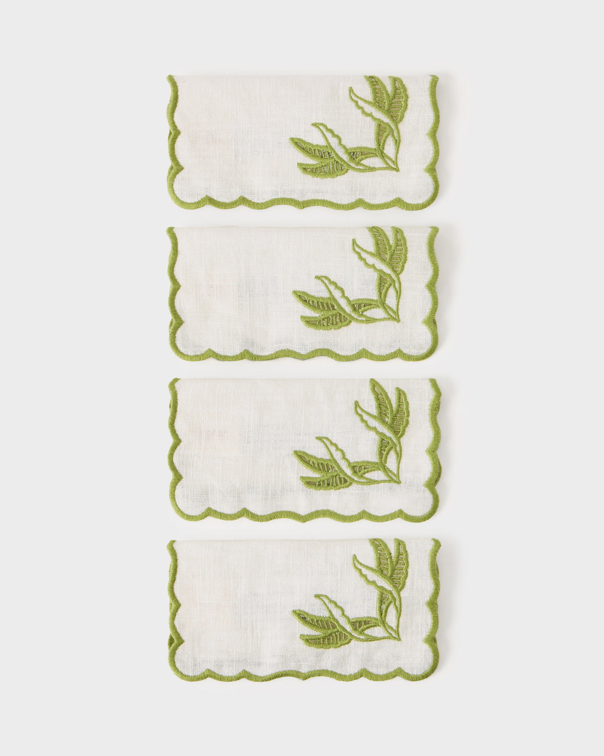 Close up of DESTREE Cabana embroidered cocktail napkins showcasing green floral embroidery and scalloped edges on a white background