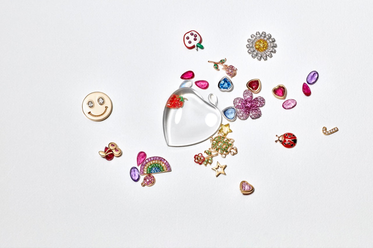 Overhead view of Blue Sapphire Heart Charm showcasing a blue sapphire in 18K gold among colorful charms on a white background