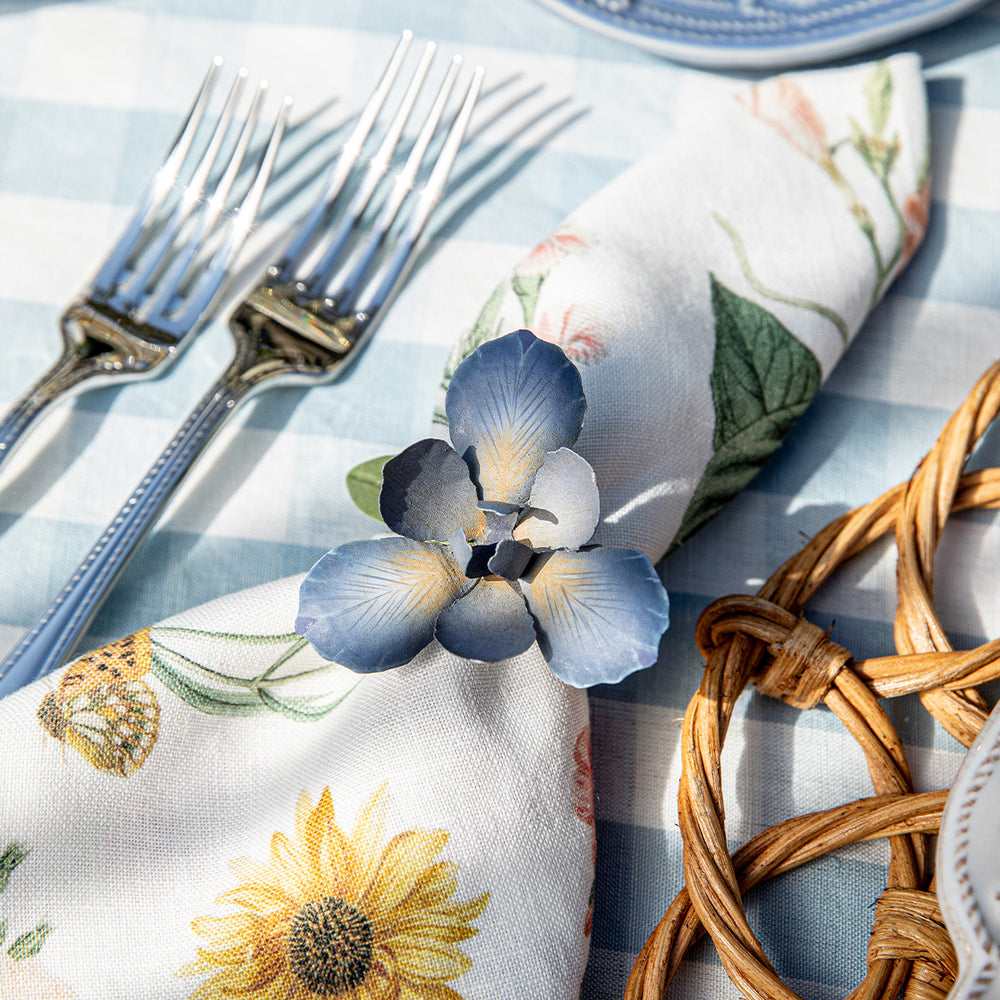 Close up of Meadow Walk Iris napkin ring in chambray showing hand painted blue iris on gold tone ring on blue gingham cloth