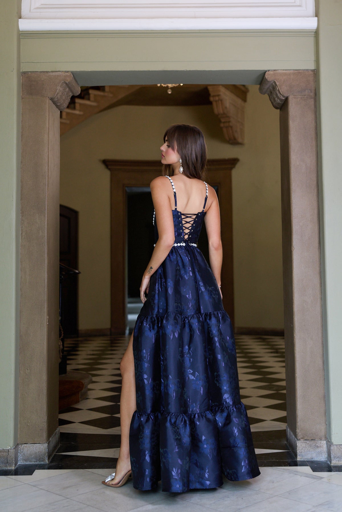 Back view of The Lucetta Dress with Beads in Navy Baroque Floral showcasing corset lacing and tiered skirt in ornate interior
