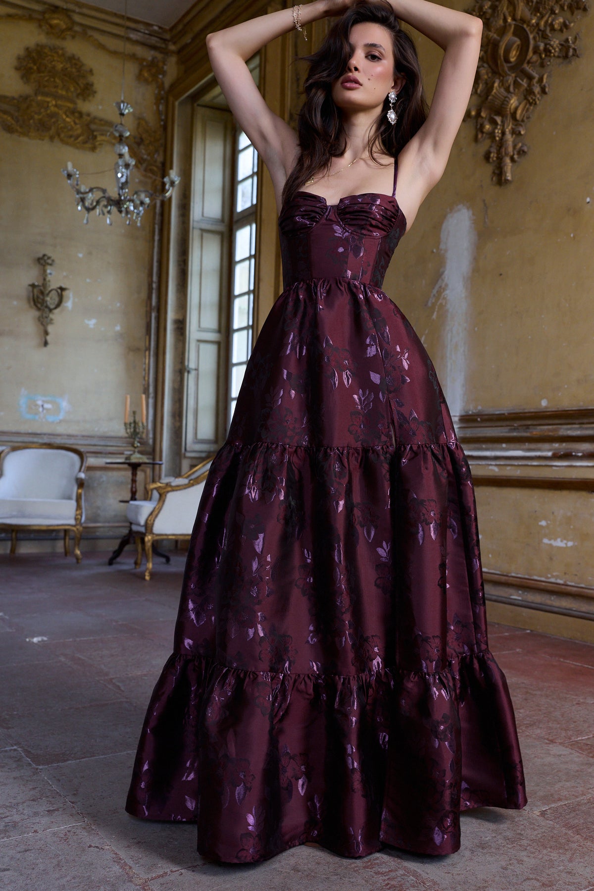 Front view of The Lucetta Dress in Plum Baroque Floral showcasing corseted bodice and tiered skirt in an ornate room