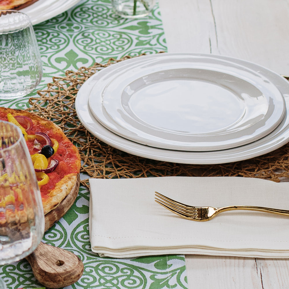 Stacked top view of Luna Salad Plate showing glossy off white glaze and raised rim on a woven placemat over green patterned tablecloth