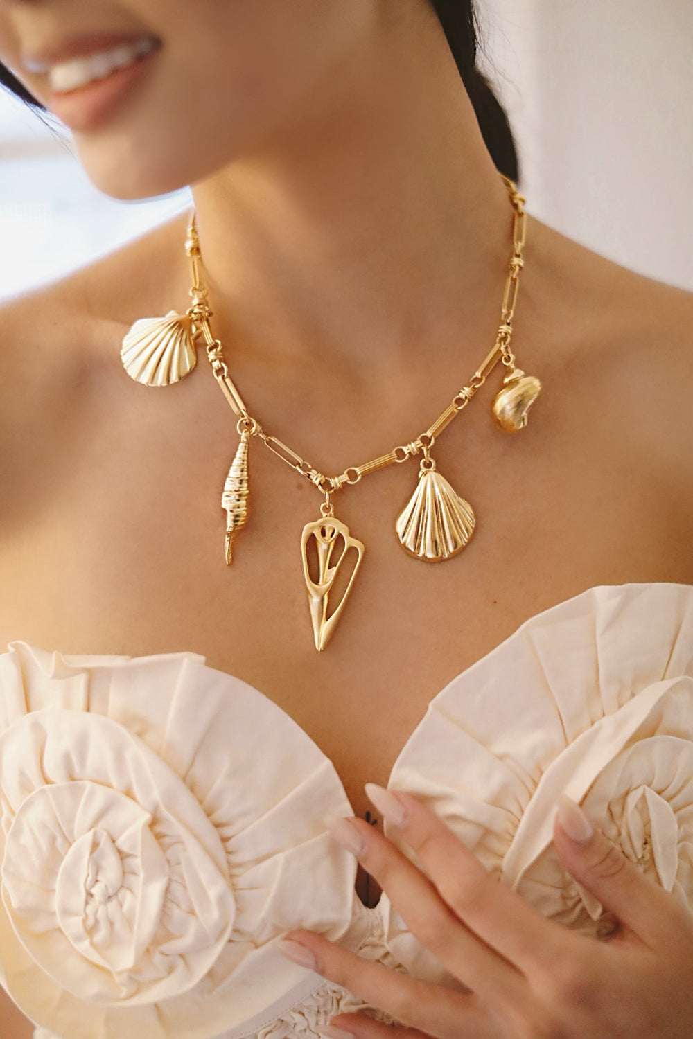 Close-up of La Mer Necklace on model showing 24K antique gold-plated chain with five seashell charms against a cream bodice