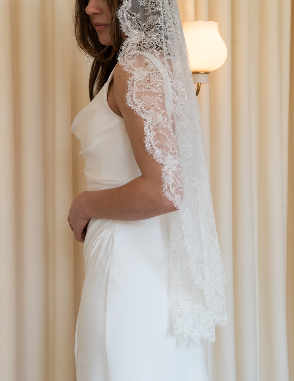 Side view of Lace Mantilla Veil showcasing scalloped Chantilly lace edging and fingertip-length drape against cream curtain backdrop