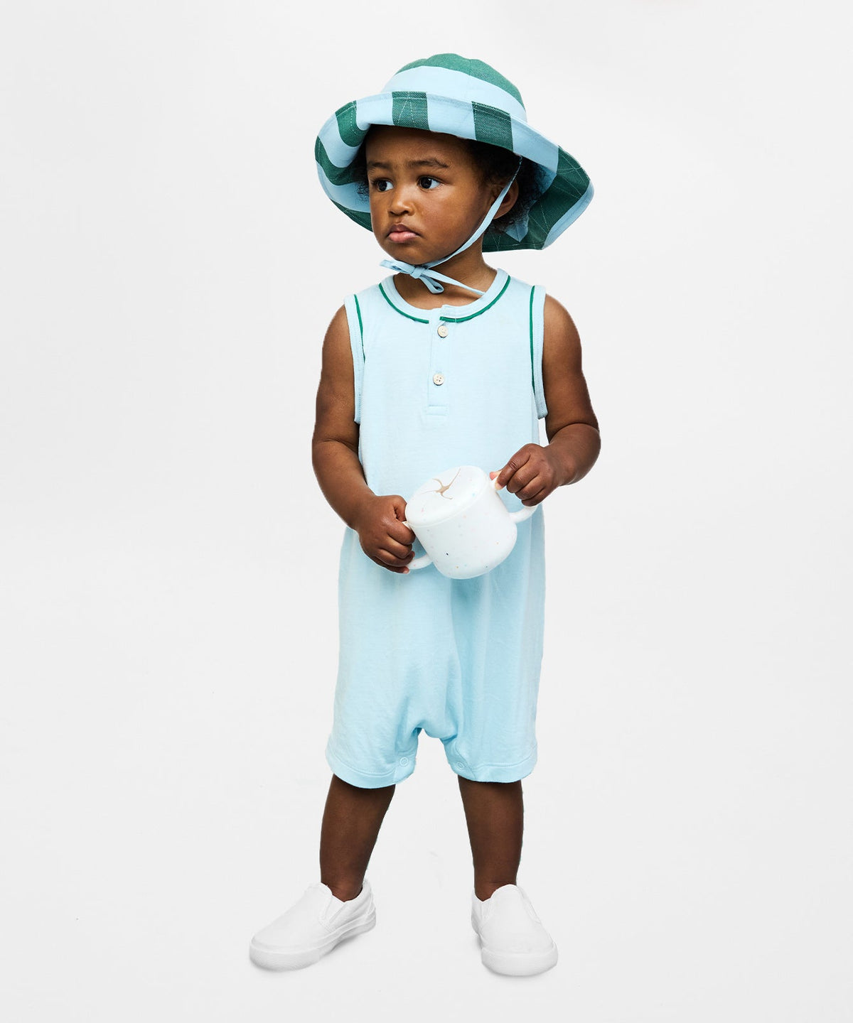 Front view of Lachlan Romper in Mist on model, sleeveless with green contrast piping and stacked buttons, white background