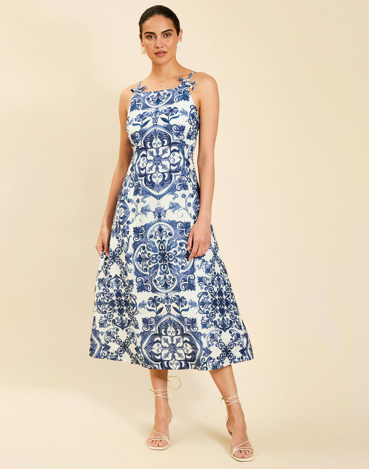 Woman wearing the Mestiza Ladera Midi Dress in Azulejo Navy print, featuring a fitted bodice, full A-line skirt, straight-across neckline, adjustable straps, side seam pockets, and linen organza fabrication.