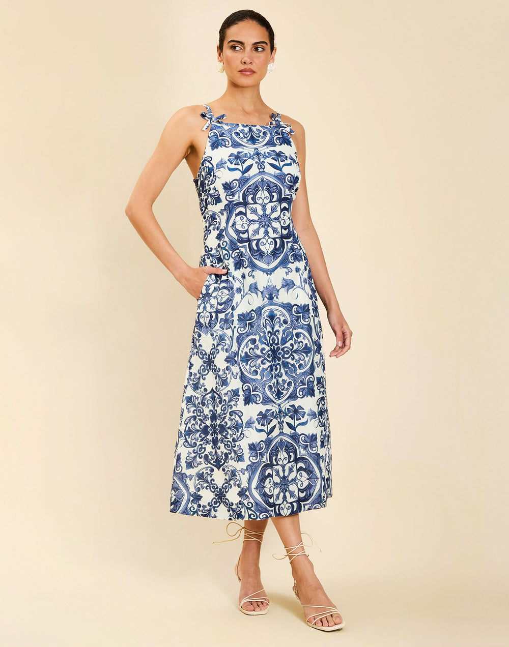 Woman wearing the Mestiza Ladera Midi Dress in Azulejo Navy print, featuring a fitted bodice, full A-line skirt, straight-across neckline, adjustable straps, side seam pockets, and linen organza fabrication.