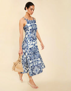Woman wearing the Mestiza Ladera Midi Dress in Azulejo Navy print, featuring a fitted bodice, full A-line skirt, straight-across neckline, adjustable straps, side seam pockets, and linen organza fabrication.
