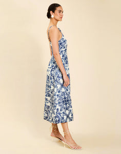 Woman wearing the Mestiza Ladera Midi Dress in Azulejo Navy print, featuring a fitted bodice, full A-line skirt, straight-across neckline, adjustable straps, side seam pockets, and linen organza fabrication.