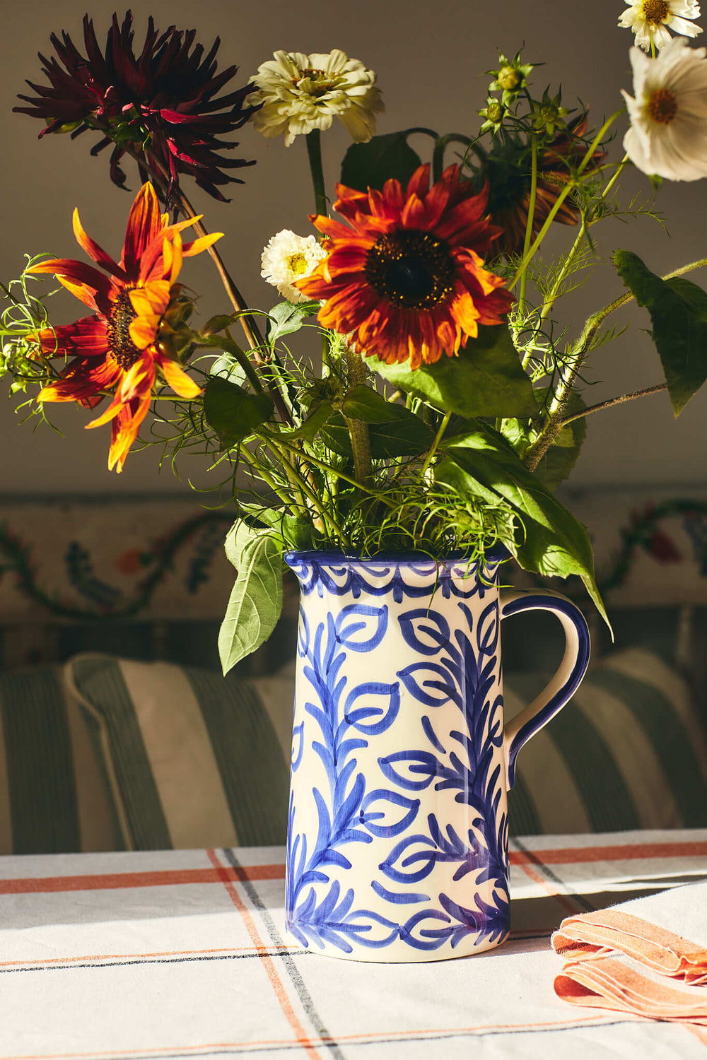 Three quarter view of Large Blue Jug showcasing hand-painted blue repintado leaf motif and handle, styled with wildflowers on a striped tablecloth