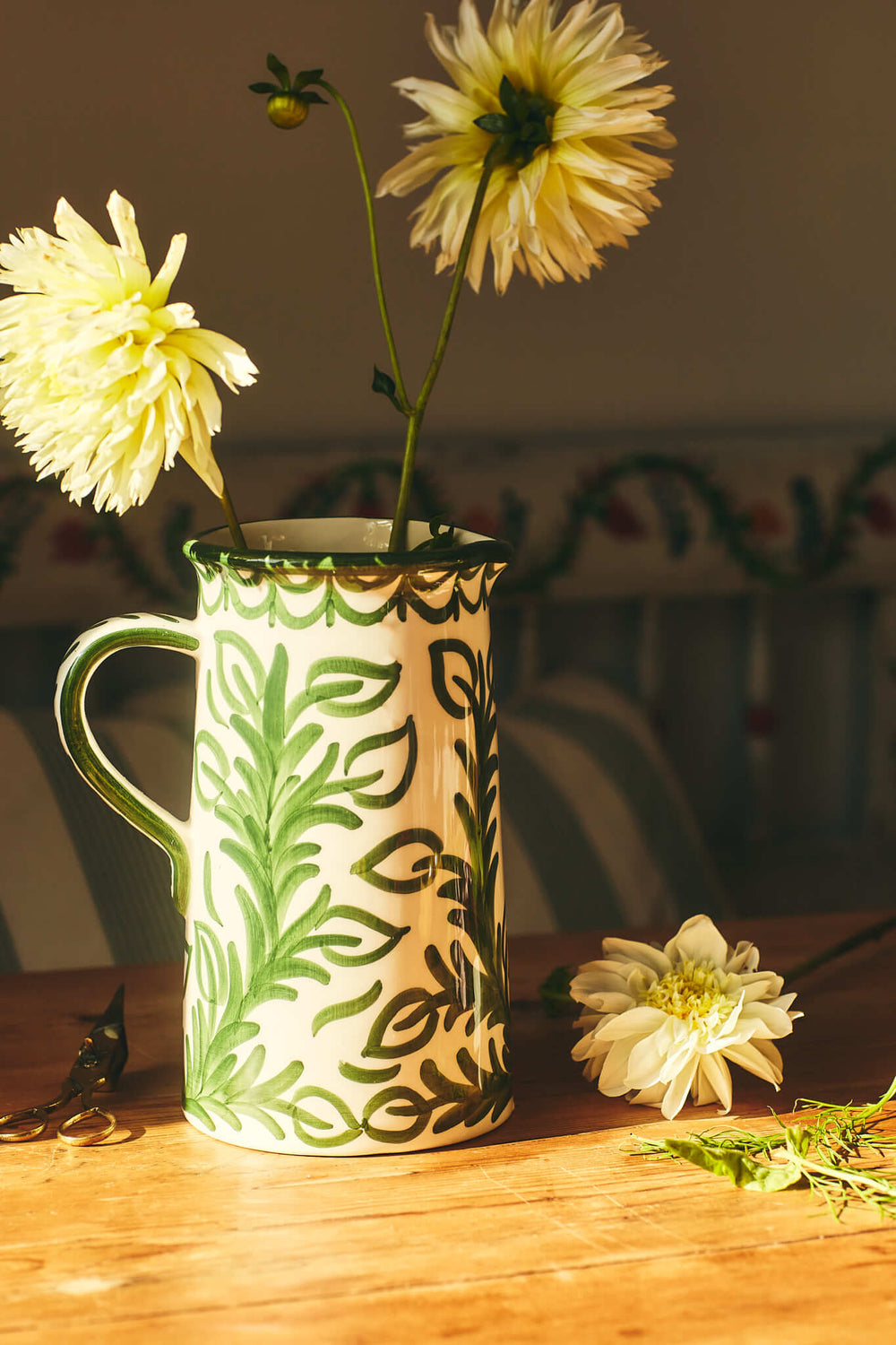 Front view of Large Green Jug showcasing hand-painted green leaf repintado motif and handle on a sunlit wooden table with white flowers