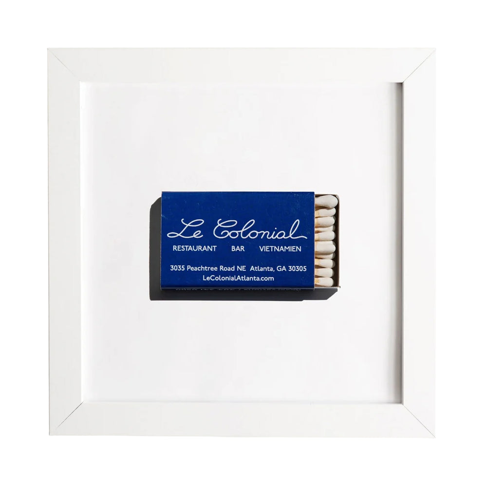Front view of framed Le Colonial matchbook print showcasing a blue matchbox centered in a white frame on a white background