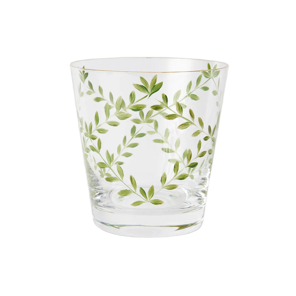 A product photograph of a clear glass tumbler with a subtle tapered shape and a gold rim, shown against a light gray background. The front of the glass is delicately hand-painted with a botanical design featuring slender, arching green branches and delicate leaves arranged in an elegant, symmetrical wreath formation.