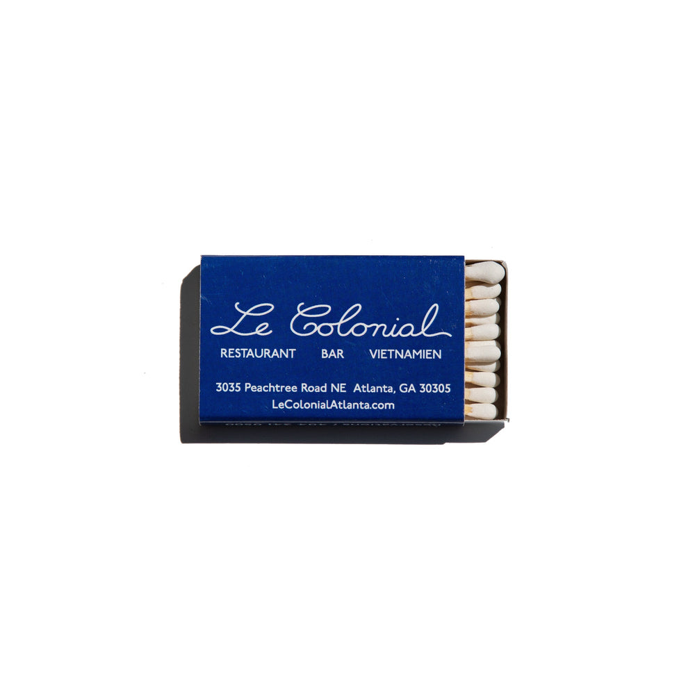 Top view of Le Colonial matchbook print showing a blue matchbox with white script and exposed matches on a white background