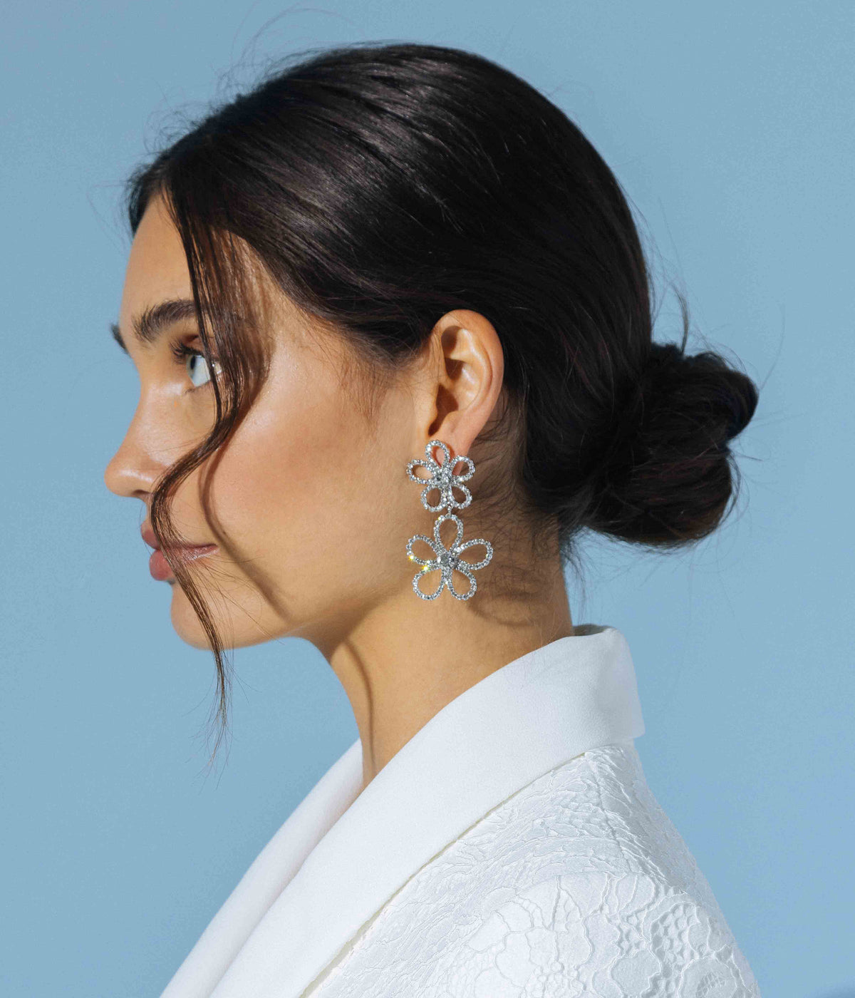 Side view of Leilani Flower Drop Earrings showcasing flower shaped drops with glass stones on model against blue background