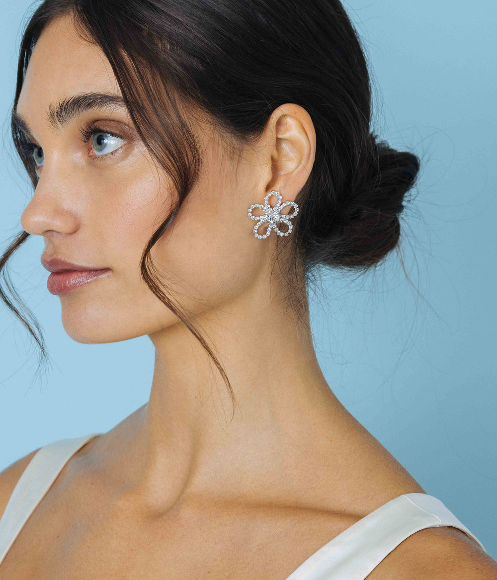 Side profile of model wearing Leilani Flower Studs showcasing silver finish flower design with CZ stones on light blue background
