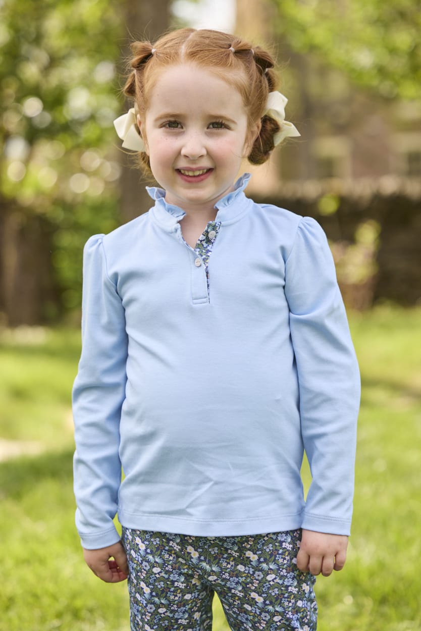Little English traditional children's clothing.  Long sleeve Hastings polo in light blue with ruffle collar and green floral detailing. Paired with green floral leggings for little girls.  
