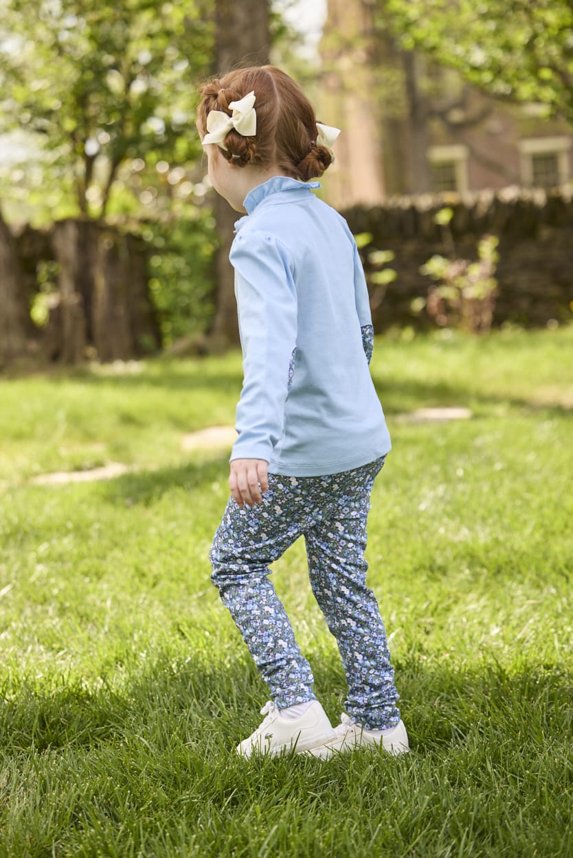 Little English traditional children's clothing.  Long sleeve Hastings polo in light blue with ruffle collar and green floral detailing. Paired with green floral leggings for little girls.  