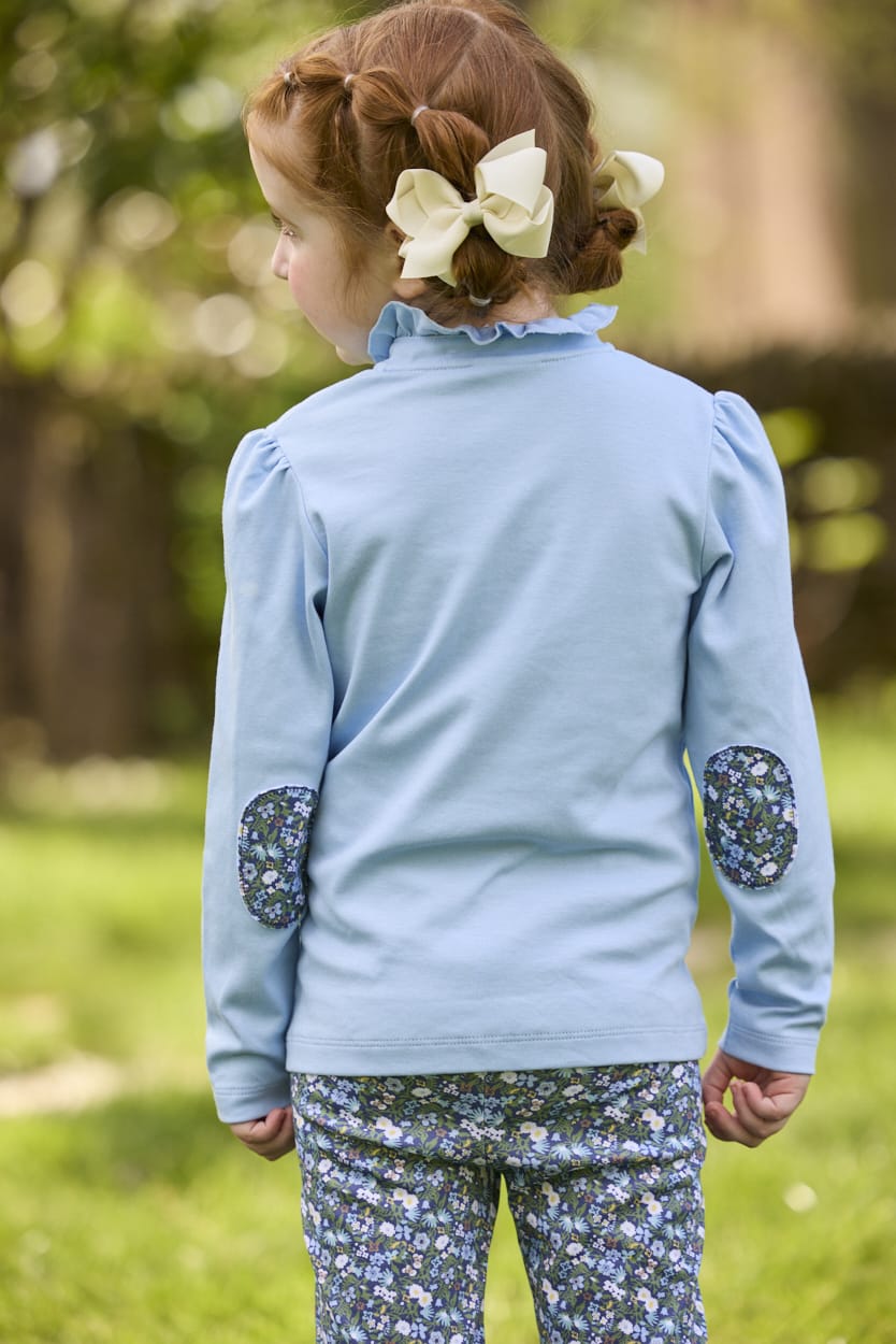 Little English traditional children's clothing.  Long sleeve Hastings polo in light blue with ruffle collar and green floral detailing. Paired with green floral leggings for little girls.  