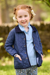 Little English traditional children's clothing.  Long sleeve Hastings polo in light blue with ruffle collar and green floral detailing. Paired with green floral leggings for little girls with navy quilted jacket layered over