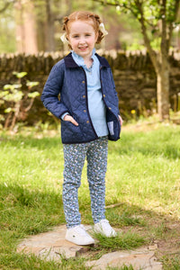 Little English traditional children's clothing.  Long sleeve Hastings polo in light blue with ruffle collar and green floral detailing. Paired with green floral leggings for little girls with navy quilted jacket layered over