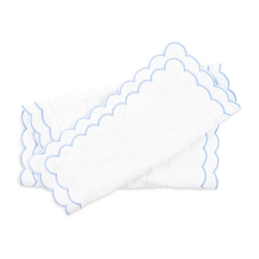 Angled folded view of Loulou Bath Mat showcasing blue scalloped double-edge embroidery on white cotton against white background