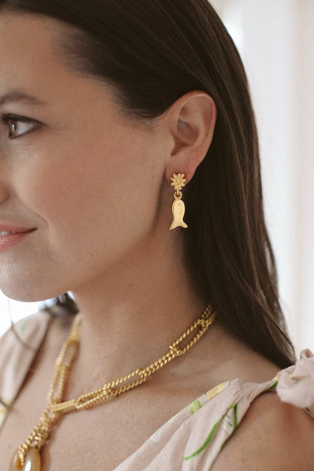 Side view of Lucky Catch Earrings showing 24K gold-plated fish charms hanging from floral studs on a model’s ear