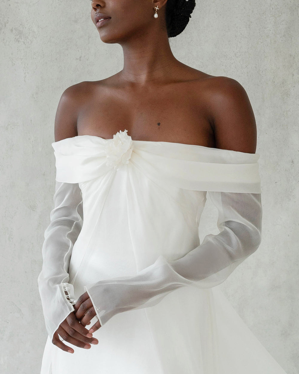 Front view of Ludlow Flower silk organza rosette worn at center bust on off-the-shoulder white gown with sheer long sleeves