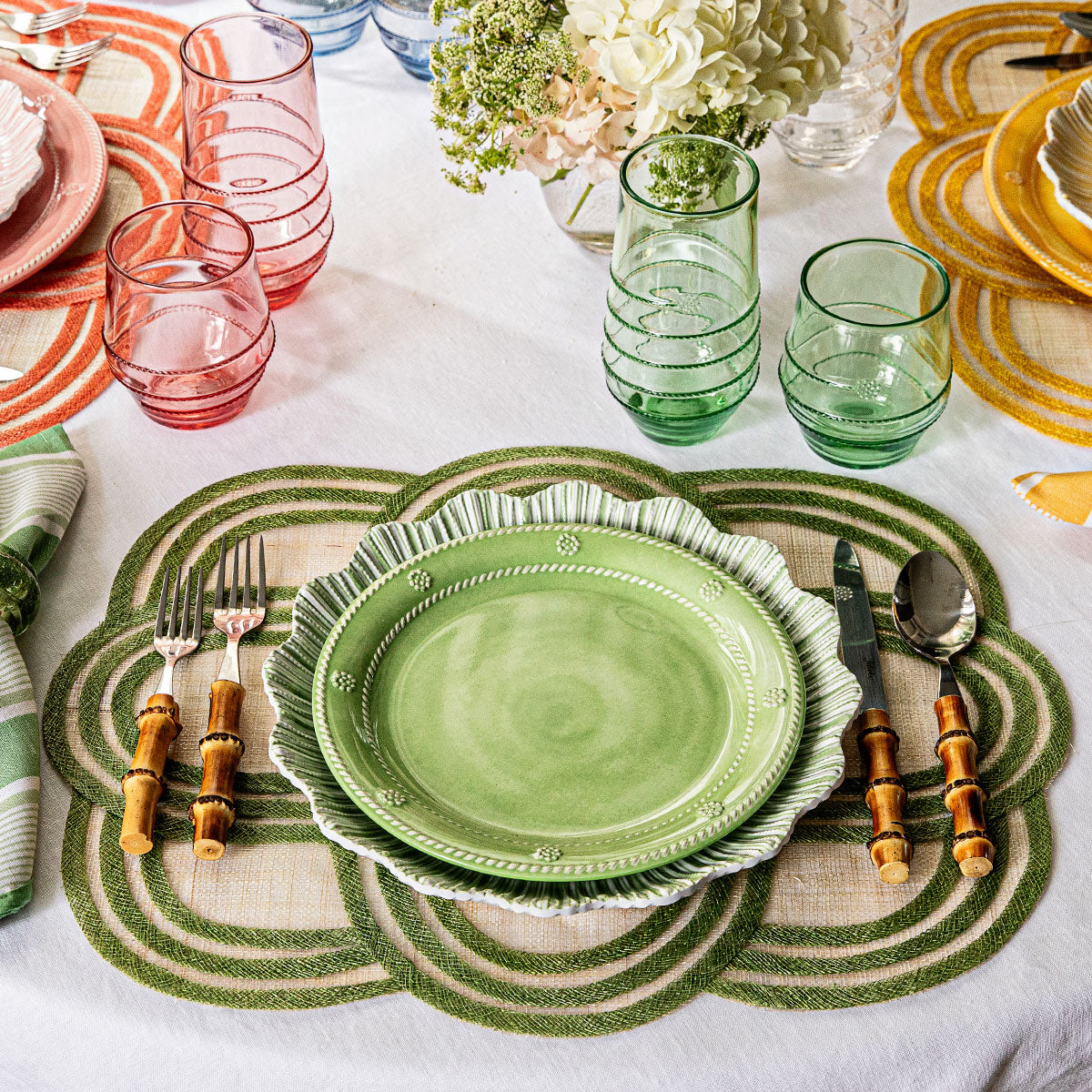 Top-down view of Berry and Thread seagrass melamine dessert plate with scalloped rim and berry-and-thread motif on a green woven placemat