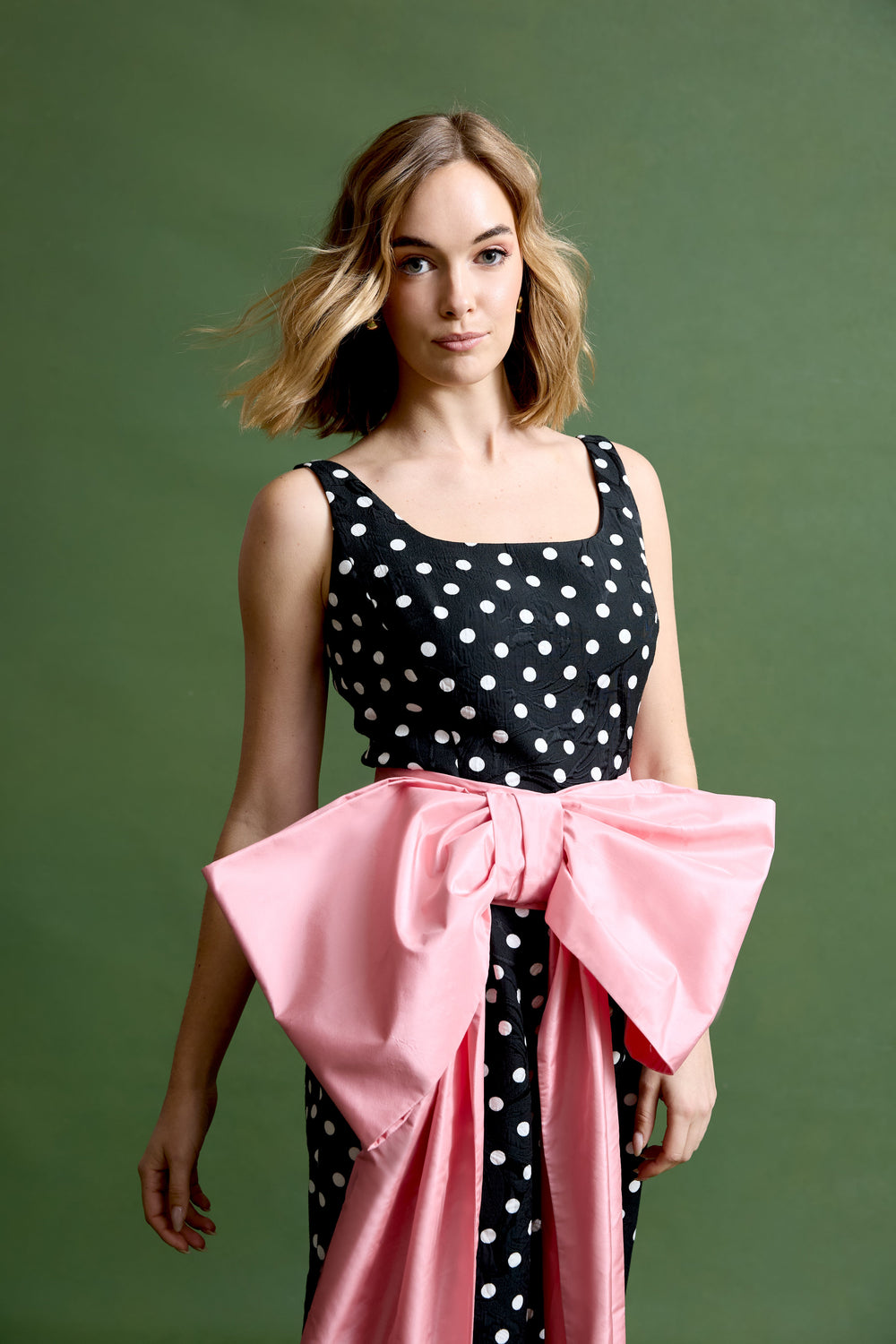 Front view of bow cummerbund with large pink satin bow tied at waist over black polka dot dress on green background