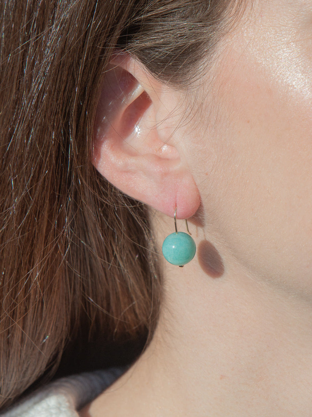 Close-up of Margot earring on model’s ear showcasing round amazonite bead on gold-filled French hook against neutral background
