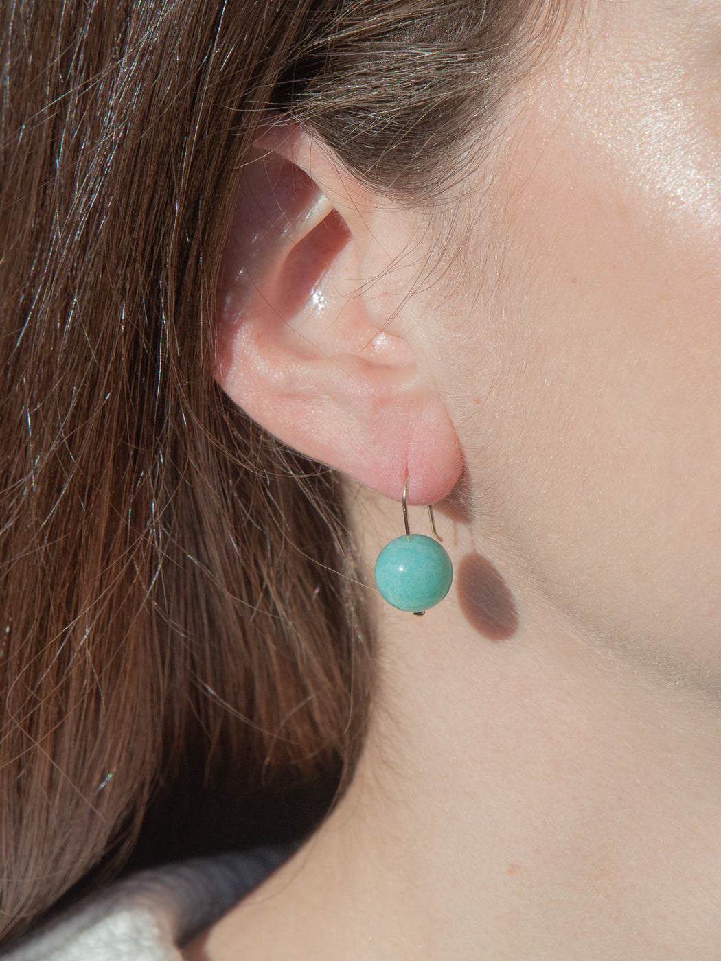 Close-up of Margot earring on model’s ear showcasing round amazonite bead on gold-filled French hook against neutral background