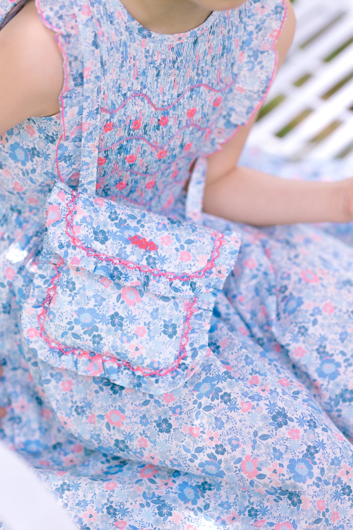 Close-up of Marguerite Floral Purse in Blue showcasing its blue floral cotton fabric and pink trim against a blurred background