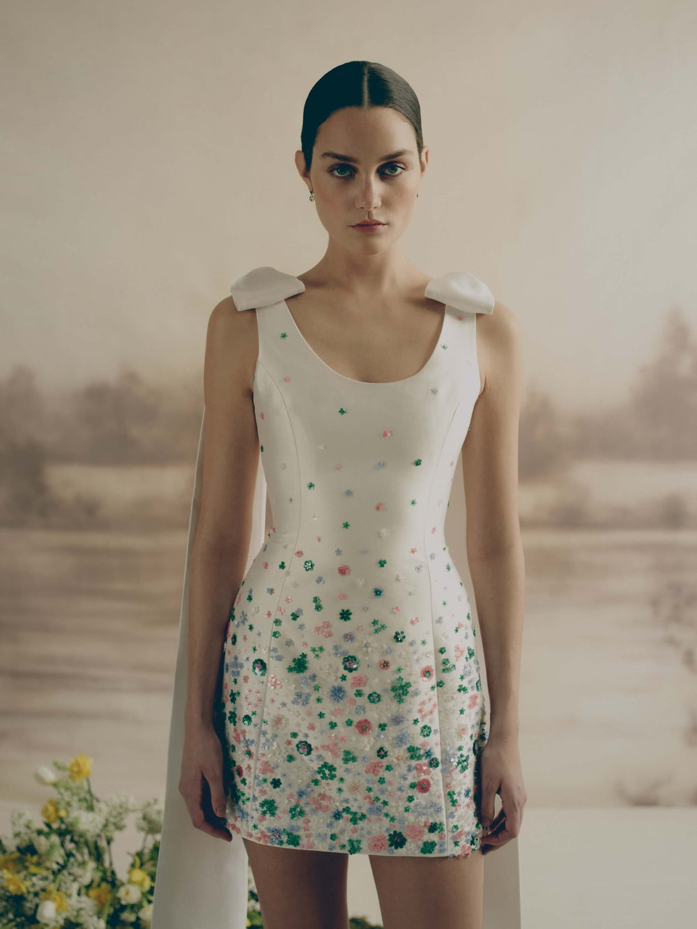 Front view of Daffodil Dress, white mini with multicolor floral beading and bow shoulder trains