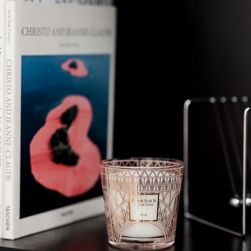 Front view of Baobab Paris candle in a gold and powder-pink silkscreen glass vessel on a table beside an art book