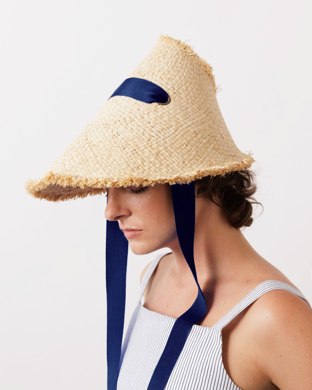 Side view of Megaphone Hat in Natural/Navy showcasing its cone-shaped raffia design and navy ribbon ties on a model