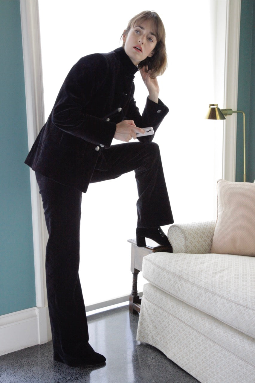 Three-quarter view of Lexi Nuit Soiree cotton velvet pants on model showcasing high-rise fit with flared leg beside sofa