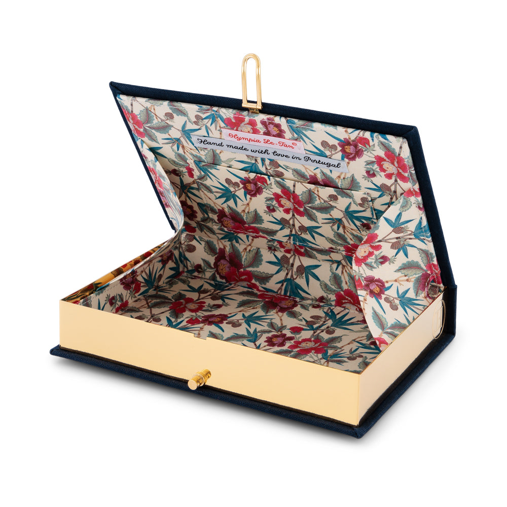 Angled open view of Fortune Teller book clutch showcasing floral interior lining and gold metal frame on white background