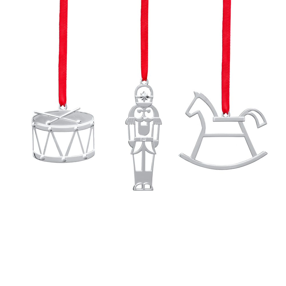Front view of three silver mini ornaments, drum, nutcracker, and rocking horse, with red ribbons on white background