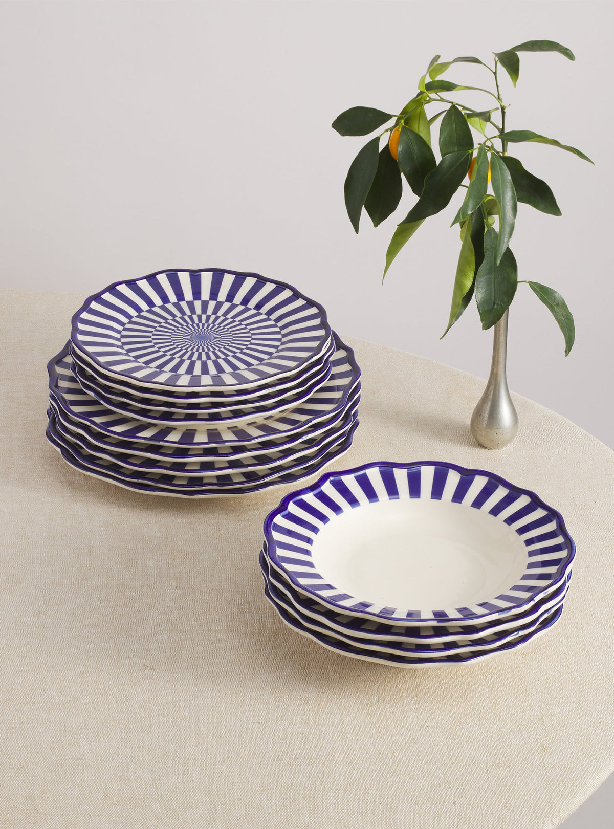 Close view of Riviera Dinnerware Set with Pasta Bowl showcasing blue and white radial stripes and scalloped edges on a linen table