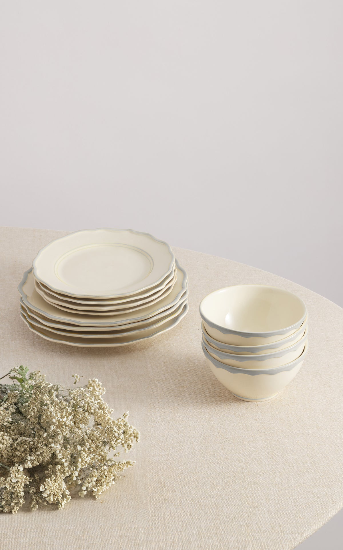 Angled view of Sylvia Dinner Plate Set of 4 showing scalloped edges and gray brushstroke rims with stacked plates and bowls