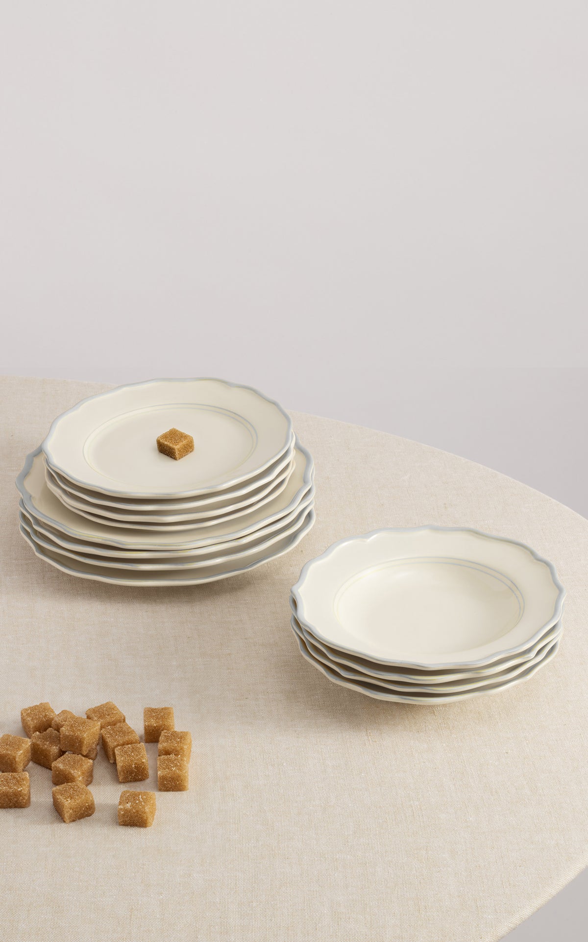 Front-angle view of Sylvia 12-piece dinnerware set showing scalloped edges and pale blue rim on a linen-covered table
