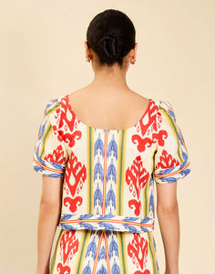 Woman wearing the Mestiza Maldives Top in Ikat Sunrise print, featuring a boxy silhouette, deep scoop neckline, pleated flutter sleeves, contrast ivory trim, and lightweight linen fabrication.