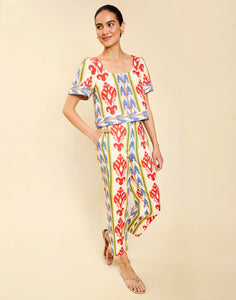 Woman wearing the Mestiza Maldives Top in Ikat Sunrise print, featuring a boxy silhouette, deep scoop neckline, pleated flutter sleeves, contrast ivory trim, and lightweight linen fabrication.
