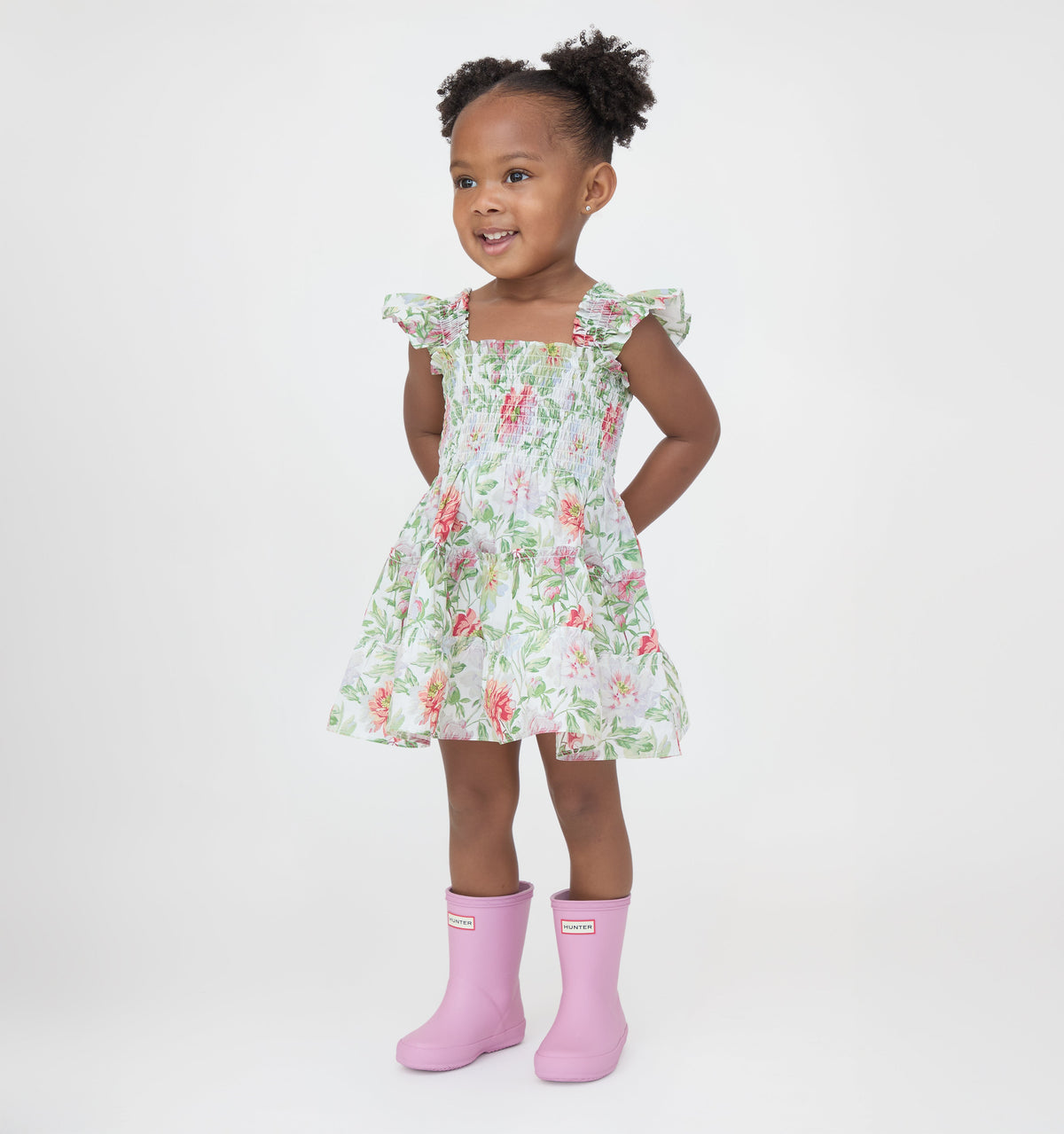 Front view of Baby Ellie Nap Dress in Peony Chintz on toddler model showcasing smocked bodice, ruffled shoulders, and knee-length floral A-line skirt on white background