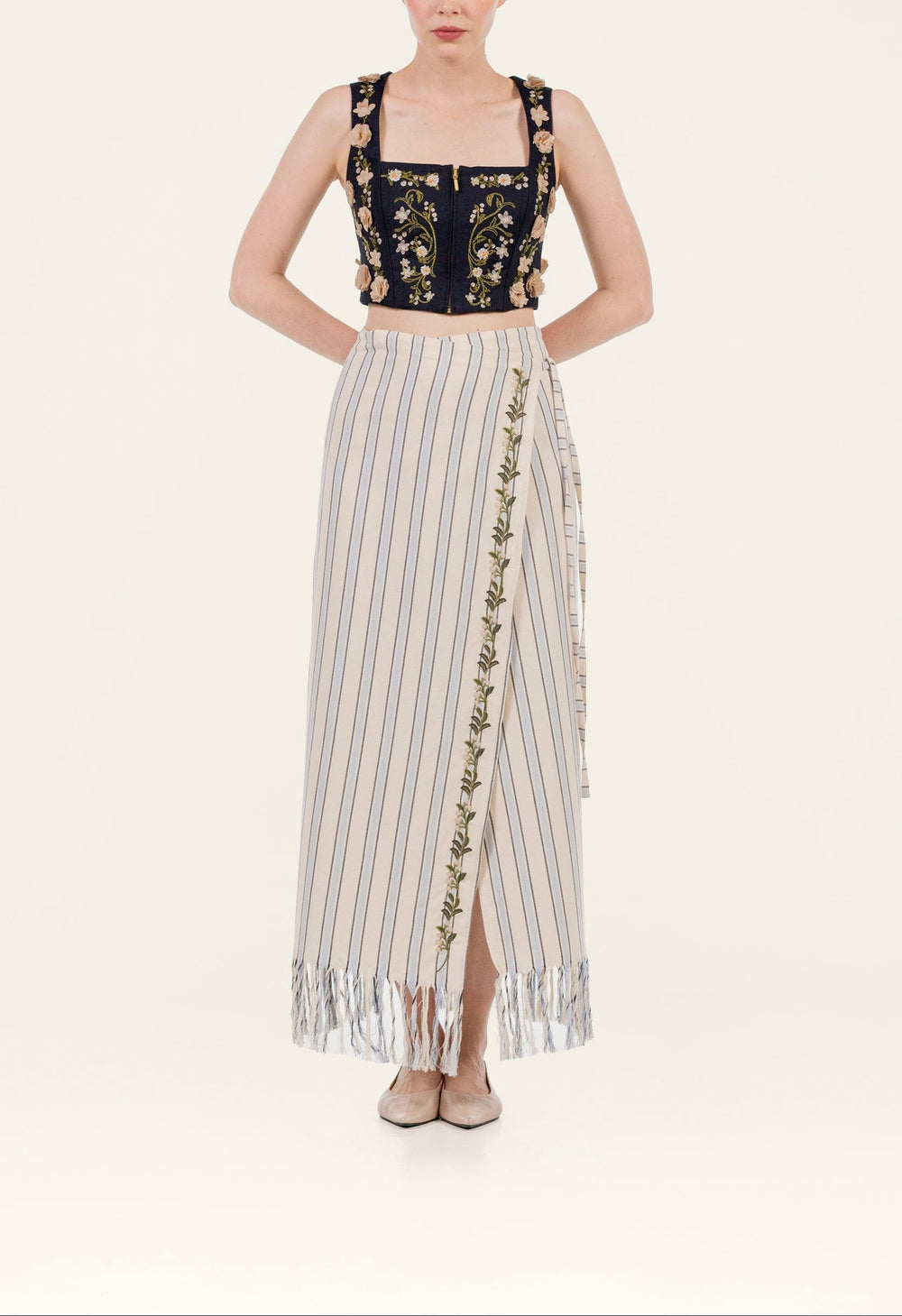 Front view of Maria Valle Pareo skirt showing vertical stripes, embroidered vine trim and fringed hem on pale background
